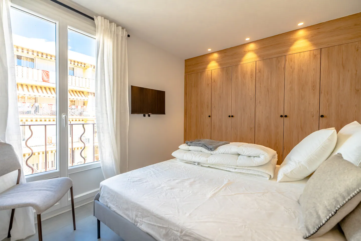 Chambre de Lei Amourie avec tête de lit en bois et rideaux blancs